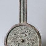 Bronze mirror with circular shape, thick raised edge, pierced central boss and handle, decorated in the centre with two heavenly creatures